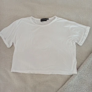 Croppad t-shirt från Pretty Little Thing - Säljer denna magtröja från Pretty Little Thing. Storlek S, fint skick utan defekter! Lite genomskinlig, men perfekt med ett spetslinne under💕