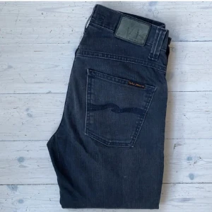 Gråa jeans från Nudie Jeans - Säljer ett par mörkgråa nudie. Modellen heter grim Tim som ni ser på 4e bilden. Skicket är bra utan defekter. Modellen på bild 5 är 180 och väger 65. Skriv för mer frågor.