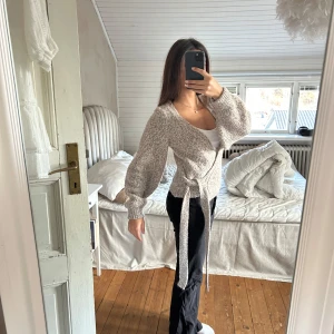 Beige stickad omlottkofta från NA-KD - Mysig beige stickad omlottkofta från NA-KD. Koftan har långa ärmar och ett knytband i midjan för en justerbar passform. Perfekt för kyligare dagar och ger en stilren look. Passar mig om vanligtvis har storlek S.