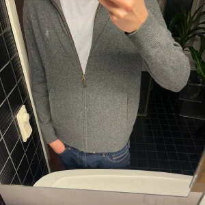 Grå kofta från Polo Ralph Lauren - Säljer en stilren grå ullkofta från Polo Ralph Lauren med dragkedja framtill. Tröjan har långa ärmar. Perfekt för en avslappnad och snygg look. 