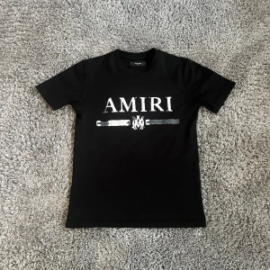 Svart t-shirt från Amiri - Snygg svart t-shirt från Amiri med ett coolt tryck på framsidan. Perfekt för en stilren look. T-shirten  är i ett exsluivt material. Byten ör intressant!
