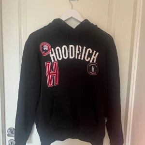 Svart hoodie från Hoodrich - Snygg svart hoodie från Hoodrich med vita och röda detaljer.