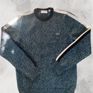 Melerad tröja från Lacoste - Säljer en stilren melerad tröja från Lacoste med långa ärmar och ribbad krage. Tröjan har en diskret logga på bröstet och kontrastfärgade ränder längs ärmarna. Perfekt för en avslappnad och trendig look.  Inga defekter. Köpt i Frankrike för 225 euro. Kom privat för mer frågor.🐊