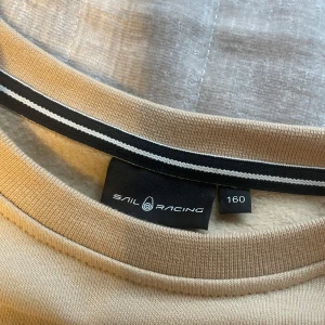 Beige färgad sail racing tröja - Säljer en beige färgad sail racing tröja endast använd en gång! Tröjan är i storlek 160 passar storlek  Xs-s. Den har inga orange ränder det är ljusets vinkel!!! Dock ser man brevid ljuset vinkel små tvåa svarta fläckar. Kanske går bort i tvätten det är iallafall på baksidan av ena armen. Hör av er vid fler frågor 💕