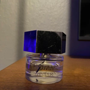 L'Homme parfym från Yves Saint Laurent - Elegant parfymflaska från Yves Saint Laurent, L'Homme. Flaskan är genomskinlig med en stilren svart text och har ett stort, geometriskt svart lock. Perfekt för den som söker en sofistikerad doft. 