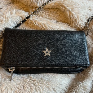 Svart axelväska med stjärndetalj - Snygg svart axelväska från gina tricot med en cool stjärndetalj på framsidan. Väskan har en kedjerem och en praktisk dragkedja upptill💕