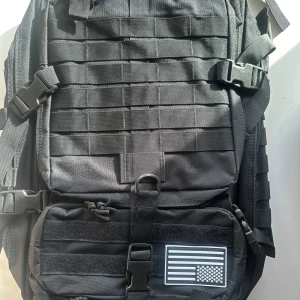 Svart ryggsäck med amerikansk flagga - Säljer en svart ryggsäck med en amerikansk flagga på framsidan. Ryggsäcken har flera justerbara remmar och spännen för optimal passform. Den är utrustad med flera fack och dragkedjor för praktisk förvaring. Perfekt för vardagligt bruk eller äventyr. Rymmer 40L 