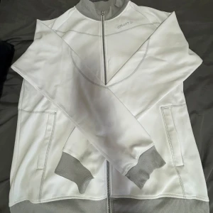 Vit jacka från Craft - Säljer en vit kofta/tröja från Craft med dragkedja. Tröjan har långa ärmar och två fickor framtill. Den har bara använts 1 gång.