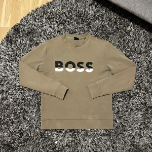 BOSS Sweatshirt - Säljer en stilren beige sweatshirt från BOSS med deras ikoniska logga i svart och vitt på bröstet. Tröjan har långa ärmar och en klassisk rund halsringning. Perfekt för en avslappnad och trendig look. Helt i ny skick! Skriv till mig för fler bilder😁Nypris är runt 1750kr och tröjan är ganska sällsynt.