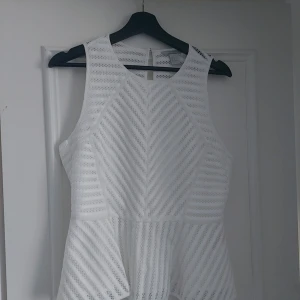 Vit ärmlös topp från H&M - Snygg vit ärmlös topp från H&M med ett diskret mönster. Perfekt för varma dagar eller som en del av en lager-på-lager look. Toppen har en lätt utsvängd form som ger en smickrande silhuett.
