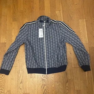 lacoste monogram kofta - Säljer en snygg mönstrad monogram sweatshirt från Lacoste i blått och vitt. Helt ny oanvänd, Storlek 5, passar som en M/L. Nypris är 2099 för denna sweatshirt jag säljer den för 1050 kronor för en HELT NY!