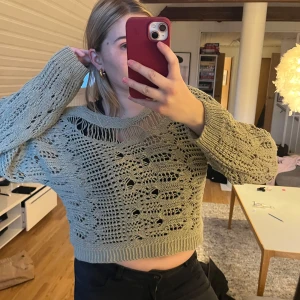 Grön stickad tröja - Säljer en snygg grön stickad tröja med ett unikt hålmönster. Tröjan är croppad och har långa ärmar med ribbade muddar. Perfekt för en trendig look! 💚