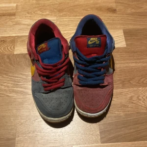 Barcelona Nike SB sneakers - Säljer ett par unika Nike SB sneakers i flerfärgad design med blå, röda och gula detaljer. Skorna har snörning och en klassisk Nike-logga på sidan. Perfekta för dig som vill sticka ut med en färgglad stil.
