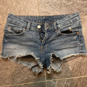 Blå jeansshorts med fransar - Snygga blå jeansshorts med fransiga kanter och slitna detaljer. Perfekta för en avslappnad sommarlook. De har en klassisk femficksdesign och knappgylf. Säljer då de börjar bli för små!💗