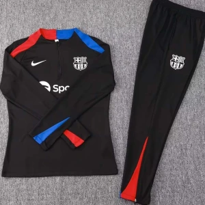 Barcelona tracksuit - Snyggt svart träningsset från Nike med klubbemblem på både tröja och byxor. Tröjan har långa ärmar med röda och blå detaljer samt en halv dragkedja framtill. Byxorna har en röd och blå rand längs benen. Perfekt för fotbollsträning eller vardagsbruk.