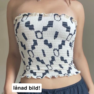 Mönstrad tubtopp  - Säljer en snygg tubtopp från H&M med ett unikt mönster i svart och beige. Toppen är smockad och har volangdetaljer vid över- och nederkant. 