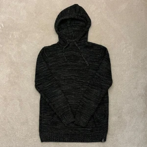Svart stickad hoodie - Säljer en svart stickad hoodie med en mysig känsla. Den har en praktisk ficka framtill och justerbar huva med snören. Perfekt för kyliga dagar.