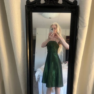 Grön axelbandslös klänning - Snygg grön axelbandslös klänning i glansigt material. Perfekt för festliga tillfällen med en elegant passform och vacker lyster. Klänningen har en dragkedja baktill för enkel påklädning.