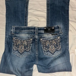 Blå jeans från Miss Me - Snygga blå jeans från Miss Me med broderade bakfickor i ett detaljerat mönster. Har dock ett hål vid innerlåret som inte syns . Har också tappat knappar på flärpen