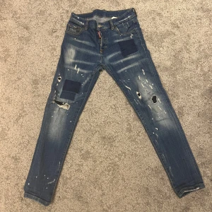 Blå jeans från Dsquared2 - Dsquared2 jeans med slitna detaljer och färgstänk. Jeansen har en klassisk femficksdesign och knappgylf | Skick 5/10 | de har ett rätt stort hål nertill men det syns ej när de sitter på 
