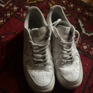 Vita Nike Air Force sneakers - Säljer ett par klassiska vita Nike Air Force sneakers. Skorna har en stilren design med perforerade detaljer på tån och snörning framtill. Perfekta för en casual look. Lite slitna men fortfarande fungerande. Nypris ca: 1500