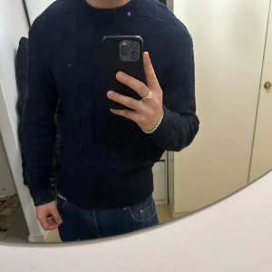 Mörkblå stickad tröja - Säljer en stilren mörkblå stickad tröja med ett diskret rutmönster. Tröjan har långa ärmar och en rund halsringning, perfekt för kyligare dagar. Nog en av mina favorit plagg jag har ägt ! Men dags och sälja vidare, väldigt fin och stilig tröja ! Passar Storlek S/M !  För mer frågor hör av er ! 💗