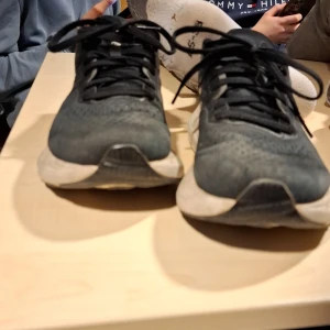 Svarta löparskor från Asics - Säljer ett par svarta Asics löparskor med snörning och vit sula. Skorna har en lätt och luftig design med Asics logotyp i silver på sidan. Perfekta för löpning och träning.