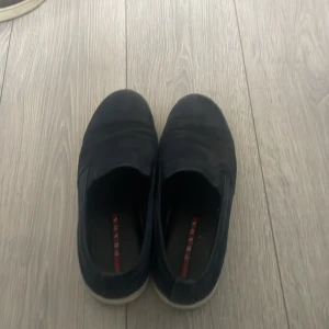 Blå loafers från Prada dom är äkta - Snygga blå loafers från Prada i mocka med en stilren design. Skorna har en vit sula och Pradas logotyp synlig både inuti och på baksidan av sulan. Perfekta för en avslappnad men elegant look.