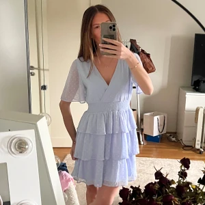 Ljusblå omlottklänning - Säljer en söt ljusblå omlottklänning med volanger och korta ärmar. Klänningen har en v-ringad design och ett prickigt mönster. Perfekt för sommarens alla tillfällen! 💙Använd fåtal gånger. Säljer för att den inte längre kommer till använd.