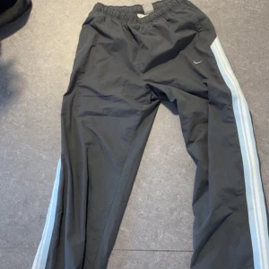 Svarta trackpants från Nike - Säljer ett par svarta trackpants från Nike med ljusblåa ränder längs sidorna. Byxorna är ganska sällsynta. Så perfekt för dig som vill sticka ut lite extra! Perfekt för många tillfällen. Tycker själv dom är sjukt snygga. Använd en gång bara. Tveka inte för frågor!