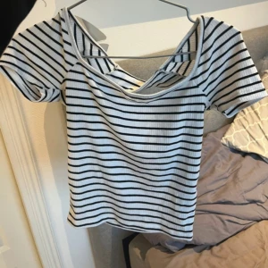 Randig ribbad topp från Gina Tricot - Säljer en snygg vit och svart randig ribbad topp från Gina Tricot. Toppen har korta ärmar och en cool desig i ryggen. Perfekt för både vardag och speciella tillfällen. I storlek S 