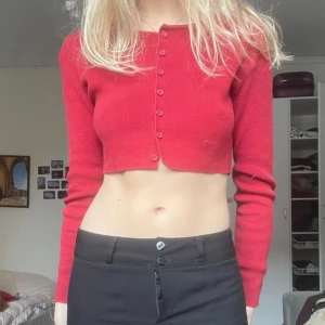 Röd croppad kofta - Säljer en snygg röd croppad kofta med knappar framtill. Perfekt för att lägga till en färgklick i din outfit. Den har långa ärmar och en tight passform som framhäver figuren. Passar bra till både jeans och kjol.