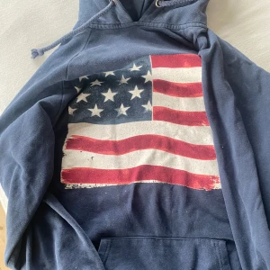 Mörkblå hoodie med amerikansk flagga från Westhill Redbird - Säljer en mörkblå hoodie från Westhill Redbird med en stor amerikansk flagga på framsidan. Storlek S