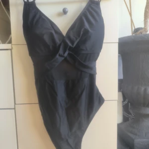 Svart baddräkt med omlott - Snygg svart baddräkt med omlott-design och v-ringad hals. Perfekt för en dag på stranden eller vid poolen. Den har justerbara axelband för bästa passform.