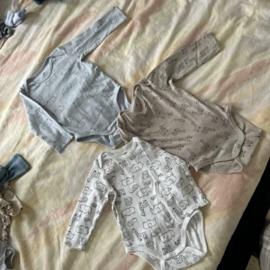 Set med tre långärmade bodys från H&M - Säljer ett set med tre långärmade bodys från H&M i ekologisk bomull. Bodysarna har söta djurmotiv i olika färger: ljusblå, beige och vit. Perfekta för små äventyrare! 🐘🦒