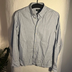 Randig skjorta Oscar Jacobson - Stilren ljusblå skjorta från Oscar Jacobson. Den hade mått bra av en strykning men jag har dessvärre inte sånna faciliteter.. Kanon-skick annars! Kika gärna andra annonser, samfrakta gärna.