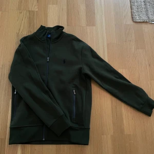 Grön track jacket från Polo Ralph Lauren - Säljer en snygg grön track jacket från Polo Ralph Lauren. Jackan har en dragkedja framtill och två praktiska fickor med dragkedjor. Använd 2 gånger annars helt ny.