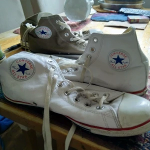 Vita Converse All Star sneakers - Klassiska vita Converse All Star sneakers med hög snörning och den ikoniska logotypen på sidan. Skorna har en vit gummisula med röd rand och en brun yttersula med mönster för bra grepp.