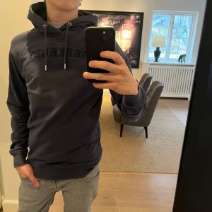 Mörkblå hoodie från Berkeley - Säljer en snygg mörkblå hoodie från Berkeley med broderad text på bröstet. Tröjan sitter svinbra på kroppen. Han på bilden är 176😁Nypris 1100kr