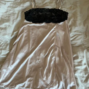 Champagnefärgad klänning från Bodyflirt - Säljer en elegant champagnefärgad klänning från Bodyflirt med svart spetsdetalj upptill. Klänningen har smala axelband och är tillverkad i polyester. Perfekt för en stilfull look.