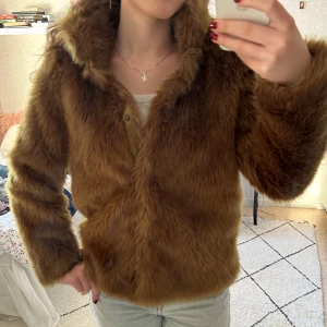 Brun pälsjacka från Vero Moda - Säljer en snygg brun/grön pälsjacka från Vero Moda. Jackan har en fluffig look med långa ärmar och en mjuk känsla. Perfekt för att hålla sig varm och stilren under kyliga dagar. Den har en klassisk design som passar till många olika outfits.