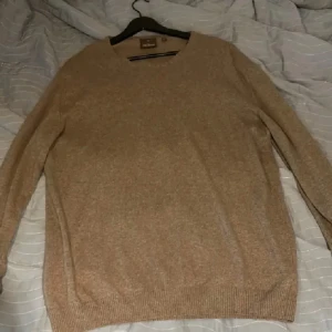 Beige stickad tröja från Oscar jacobsson - Säljer en stilren beige stickad tröja med rund hals från Oscar Jacobsson. Tröjan har långa ärmar och ribbade muddar vid ärmslut och nederkant. Strl Xl men sitter som en L. Pris går att diskutera vid snabb och smidig affär!