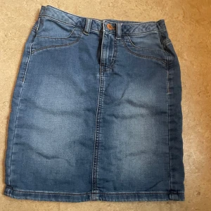 Jeanskjol från Jacqueline de Yong - Snygg jeanskjol från Jacqueline de Yong i klassisk blå denim. Kjolen fickor både fram och bak samt en knapp och dragkedja framtill. Perfekt för en avslappnad stil. (Liten för storleken, då den blivit tvättad ett par gånger)