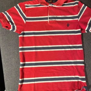 Röd och vit randig pikétröja från Morris - Säljer en snygg röd och vit randig pikétröja från Morris. Tröjan har korta ärmar och en klassisk krage med knappar framtill. Perfekt för en avslappnad stil med en touch av elegans. 140kr