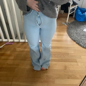 Ljusblå bootcut jeans - Säljer ett par ljusblå bootcut jeans med hög midja. Jeansen har en klassisk femficksdesign och stängs med en knapp och dragkedja. Perfekta för en avslappnad stil.