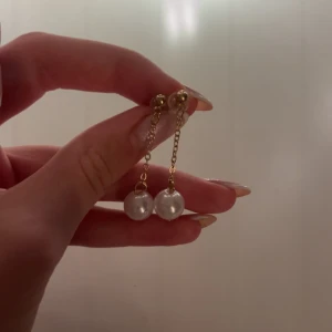 Guldörhängen med pärlor - Eleganta örhängen i guld med hängande kedjor och vita pärlor. Perfekta för att ge en sofistikerad touch till din outfit, anföring använda