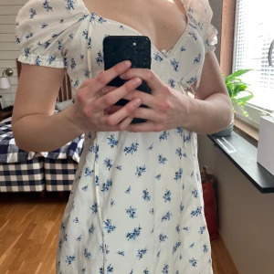 Vit blommig klänning med puffärmar - Säljer denna vita klänning med blå blommönster och puffärmar. Använd 1 gång och i mycket bra skick. 