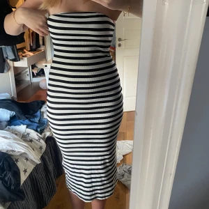 Randig axelbandslös klänning - Snygg axelbandslös klänning med svartvita ränder. Perfekt för en stilren look. Klänningen är figurnära och har en ribbad textur som ger en modern touch.