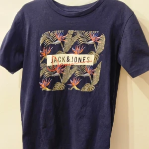 Mörkblå t-shirt från Jack & Jones - Snygg mörkblå t-shirt från Jack & Jones med ett tropiskt mönster på framsidan. Perfekt för en avslappnad stil med korta ärmar och rund hals. Tillverkad i mjukt material för extra komfort.