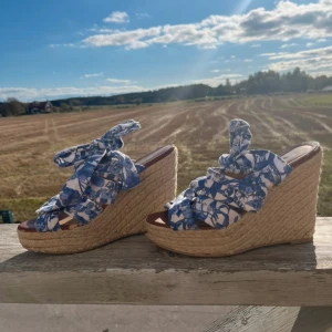 Blommiga kilklackar från H&M - Snygga kilklackar från H&M med blommigt mönster i blått och vitt. Skorna har en hög kilklack i flätad stil och knytband som ger en somrig känsla! Defekt på framsidan (se sida 4)💙 
